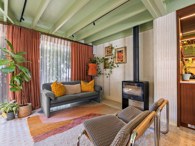 A cozy living room featuring an exposed beam ceiling, a modern freestanding fireplace, and a stylish tiled feature wall with direct access to the patio.