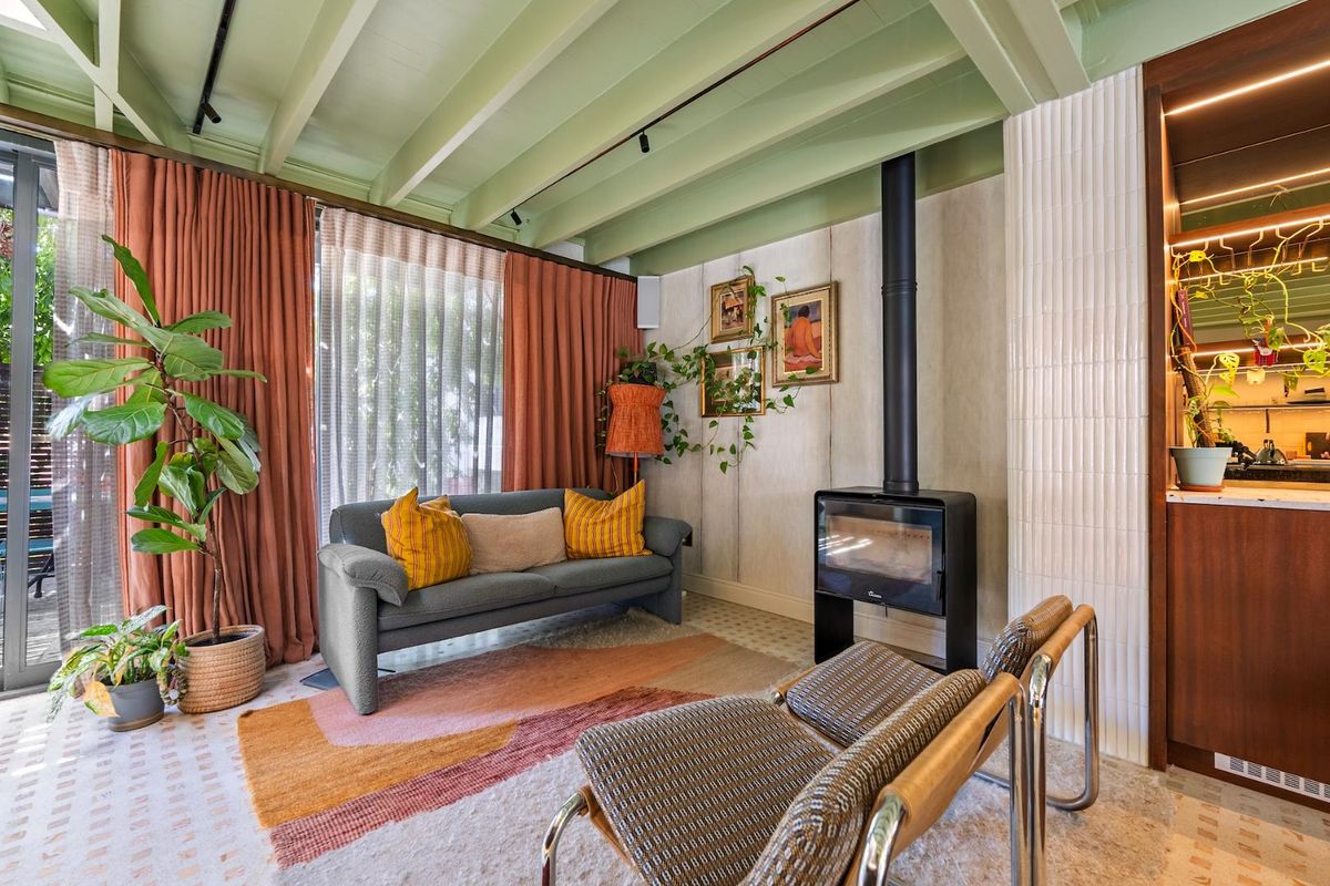 A cozy living room featuring an exposed beam ceiling, a modern freestanding fireplace, and a stylish tiled feature wall with direct access to the patio.