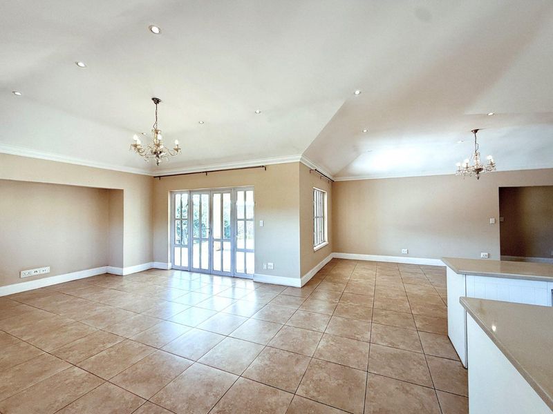 Spacious open-plan living and kitchen area featuring neutral tiled floors, recessed lighting, crown molding, and direct access to the outdoors through french doors.
