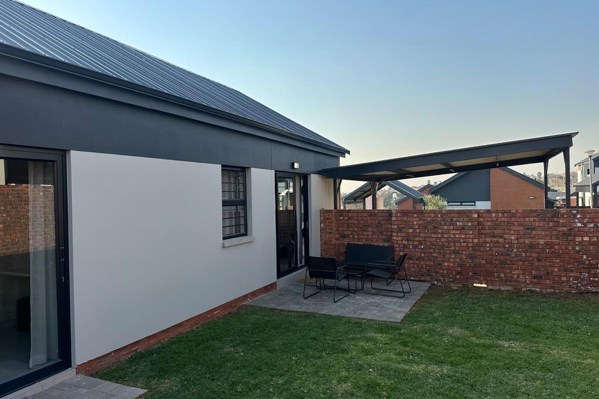Rear view of the townhouse featuring a paved patio area, covered pergola, brick boundary wall, and well-maintained lawn with modern sliding door access.