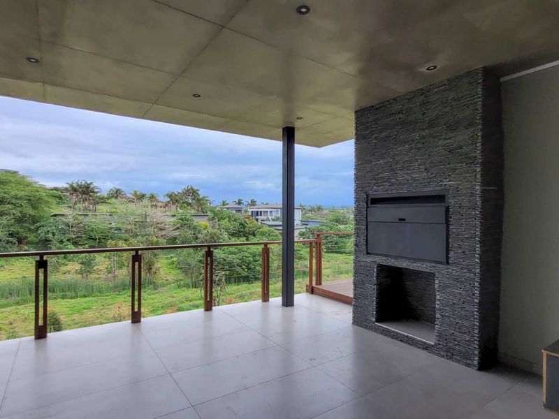Spacious covered balcony featuring a built-in stone-clad braai, modern tiled flooring, and a timber balustrade with scenic views.