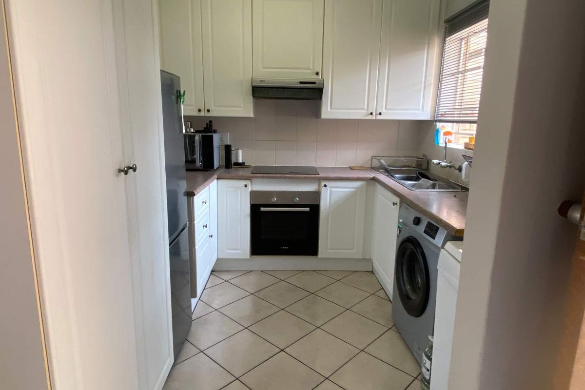 Compact kitchen featuring white cabinetry, built-in oven, electric hob, extractor fan, and tiled flooring with integrated space for laundry appliances.