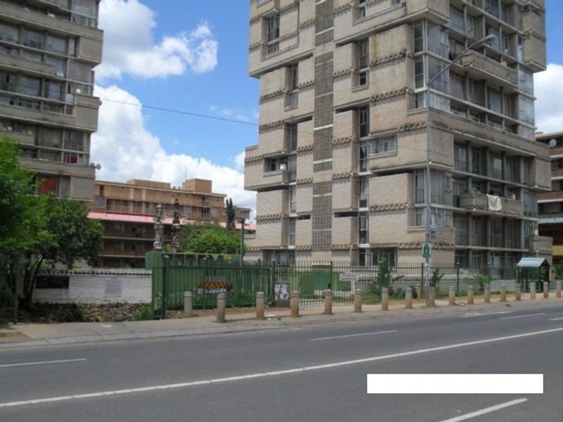 Street-level view of a multi-story apartment complex featuring brick facade construction and secure perimeter fencing along the roadside.