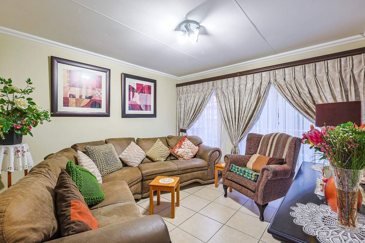 A comfortable living room featuring tiled flooring, crown molding, and large windows with draped curtains, providing a bright and inviting space.