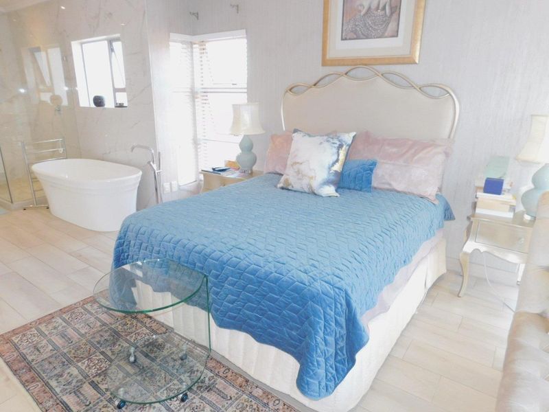 Spacious bedroom featuring an open-plan en-suite bathroom with a modern freestanding bathtub, glass shower enclosure, and contemporary tiled flooring.