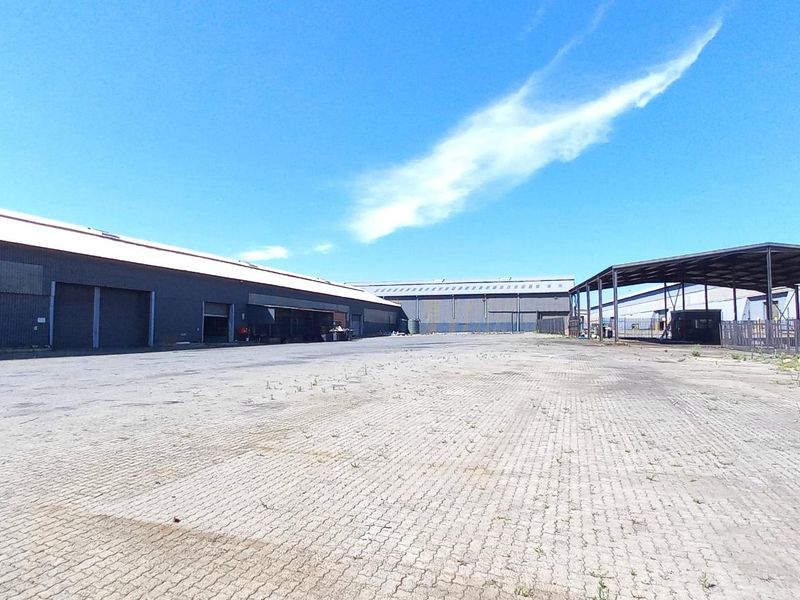 Expansive industrial yard featuring paved surfaces, metal-clad warehouse structures, and a covered loading area, suitable for logistics or storage operations.