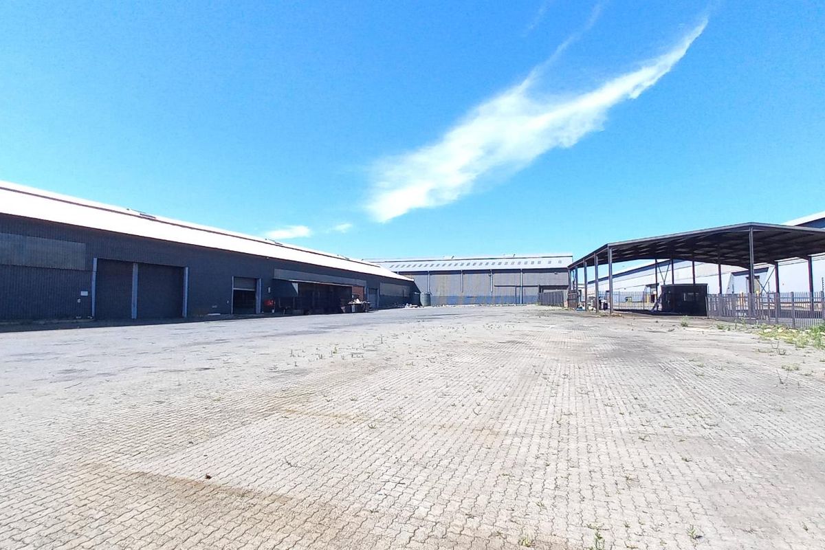 Expansive industrial yard featuring paved surfaces, metal-clad warehouse structures, and a covered loading area, suitable for logistics or storage operations.
