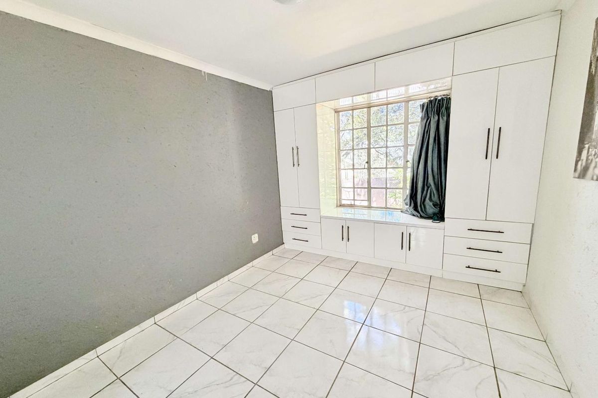 A bright bedroom featuring white tiled flooring, a large window with built-in cabinetry, and ample storage space with integrated cupboards.