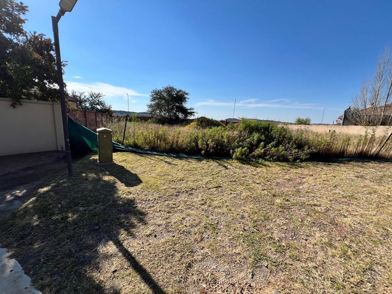 A vacant residential plot featuring a perimeter wall, utility connection, and overgrown vegetation, offering a blank canvas for future development.