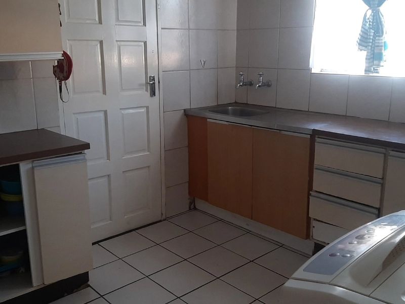 A functional kitchen featuring tiled flooring, built-in cabinetry with laminate countertops, and a stainless steel sink, offering potential for modern updates.