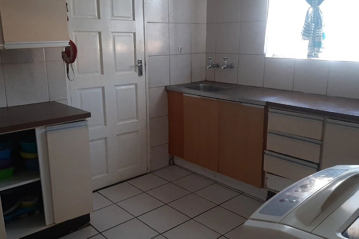 A functional kitchen featuring tiled flooring, built-in cabinetry with laminate countertops, and a stainless steel sink, offering potential for modern updates.