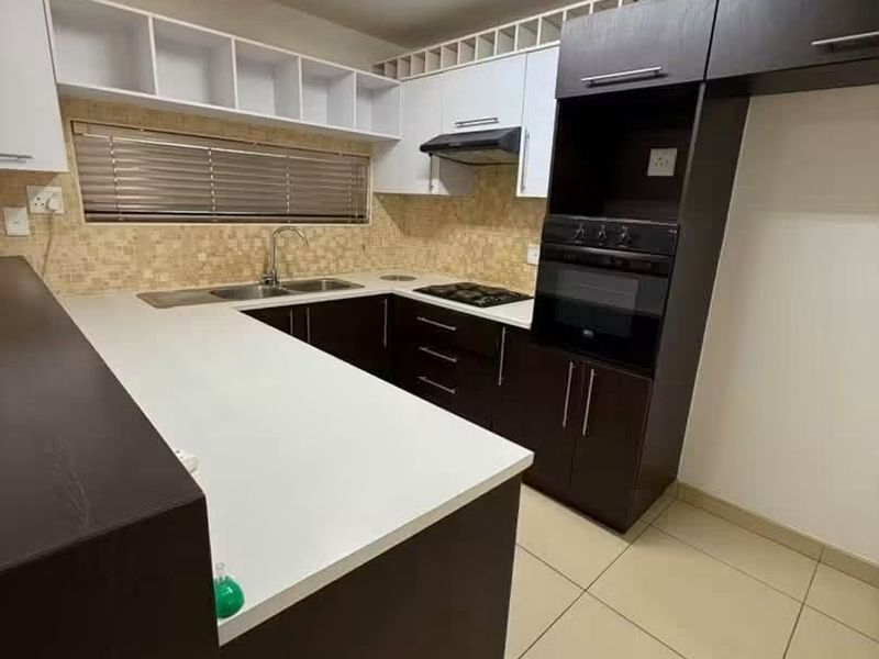 A modern kitchen featuring dark and white cabinetry, built-in oven, hob, extractor fan, and tiled backsplash with ample counter space.