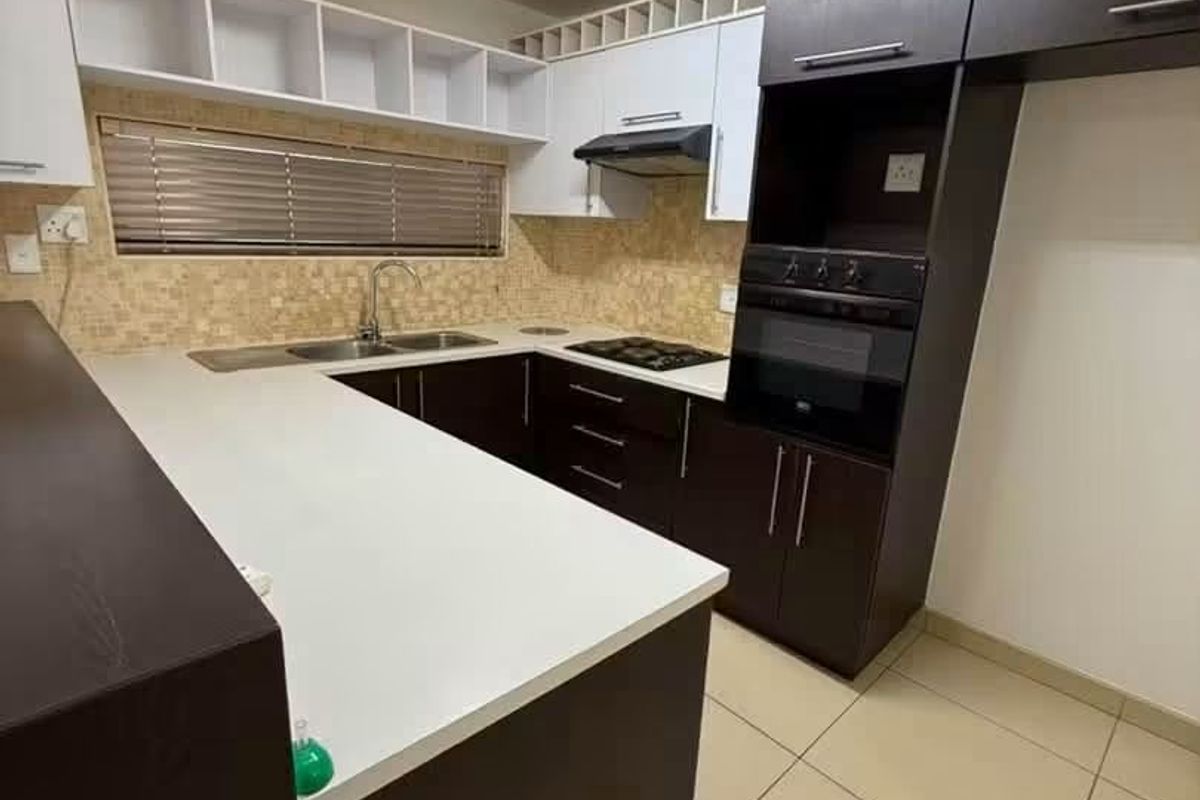 A modern kitchen featuring dark and white cabinetry, built-in oven, hob, extractor fan, and tiled backsplash with ample counter space.