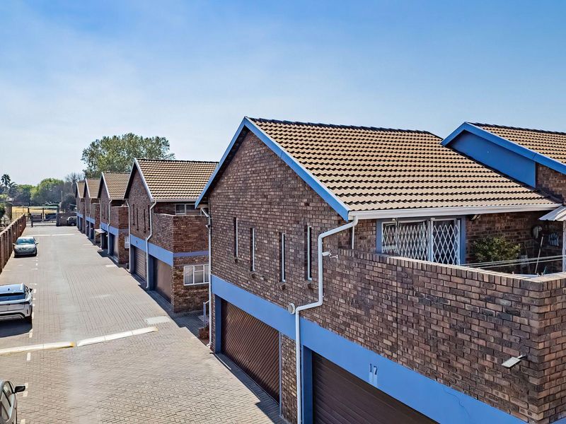 An elevated view of a residential apartment complex featuring face brick facades, tiled roofs, and paved driveway access with integrated garage doors.