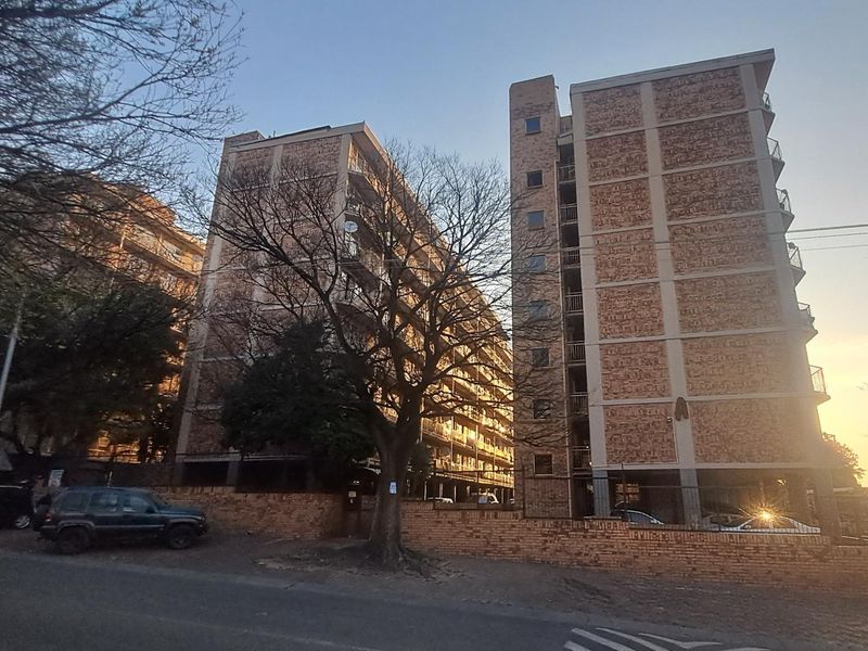 Exterior view of a multi-story brick apartment complex featuring balconies and a perimeter wall, captured during late afternoon.