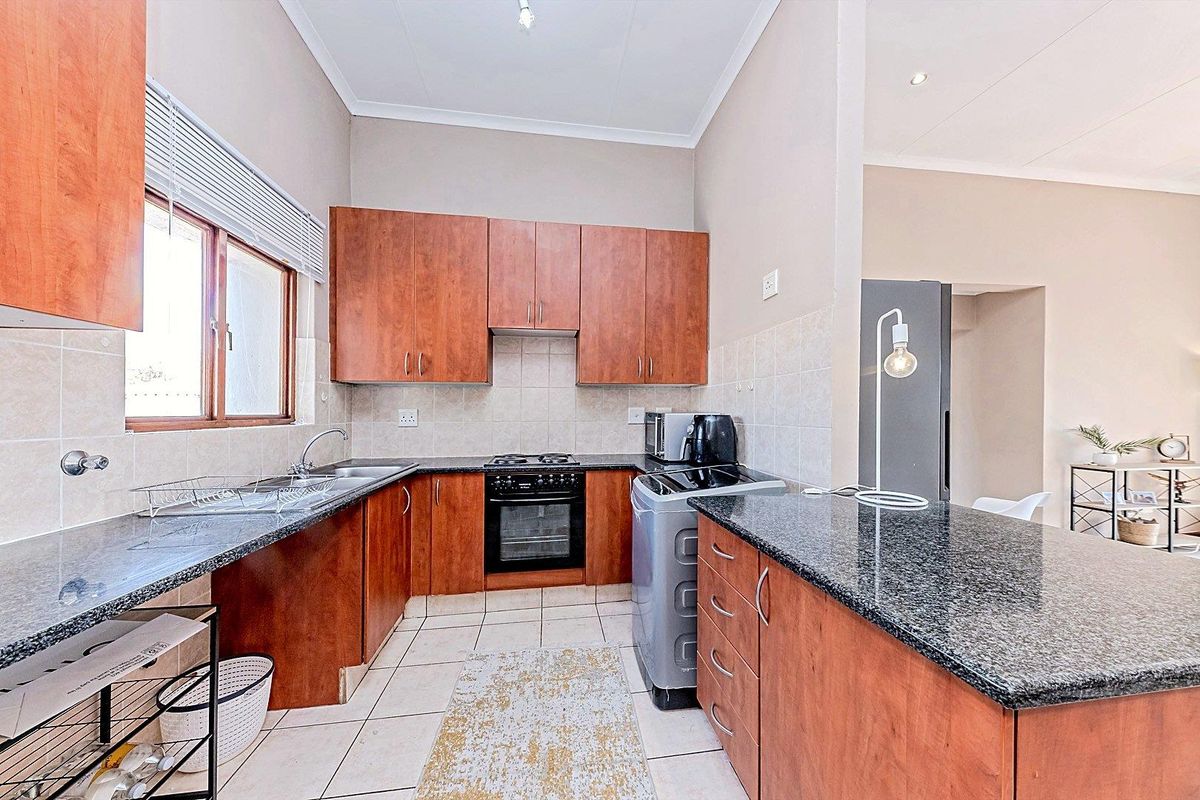 A functional kitchen featuring wooden cabinetry, granite countertops, tiled flooring, and a built-in oven with a gas hob.