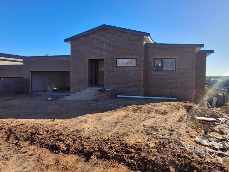 Front view of a newly constructed brick house featuring a double garage, concrete entrance steps, and an unlandscaped yard area.
