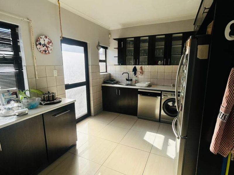 A functional kitchen featuring dark wood cabinetry, tiled backsplash, integrated dishwasher, and built-in washing machine with light ceramic floor tiles.