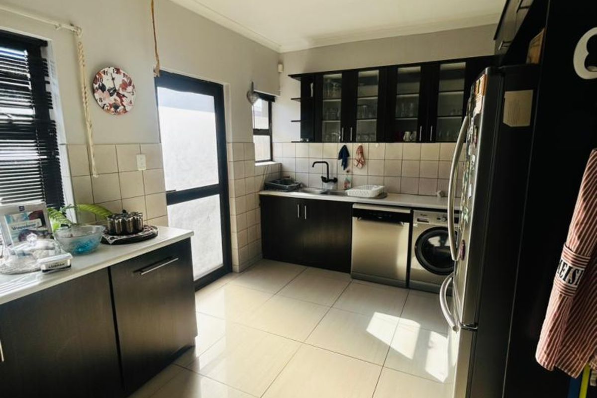 A functional kitchen featuring dark wood cabinetry, tiled backsplash, integrated dishwasher, and built-in washing machine with light ceramic floor tiles.