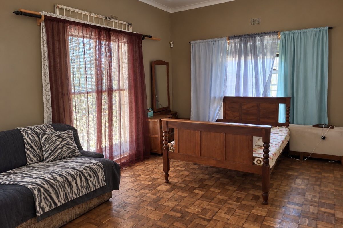 Spacious bedroom featuring traditional parquet flooring and large windows with security gates, offering a functional layout with ample natural light.
