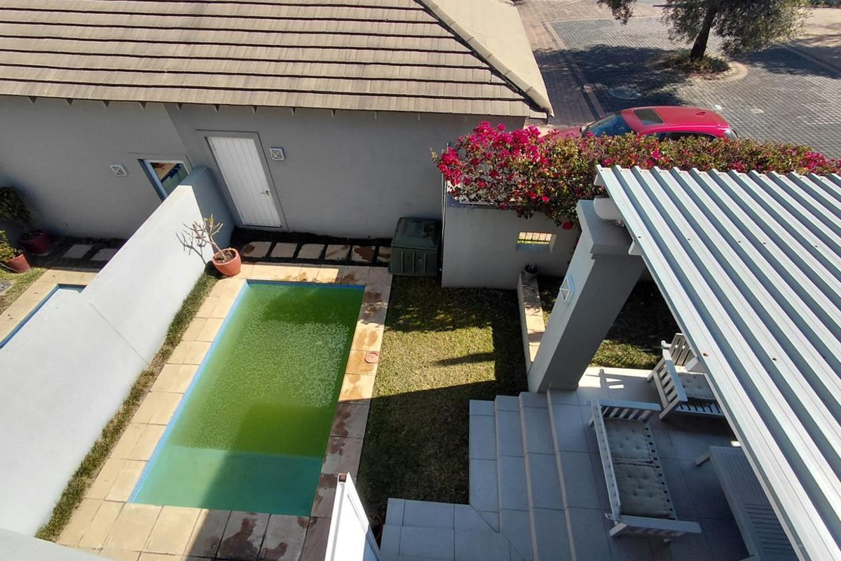 Aerial view of a cluster property backyard featuring a covered patio, small garden, and a swimming pool requiring maintenance.