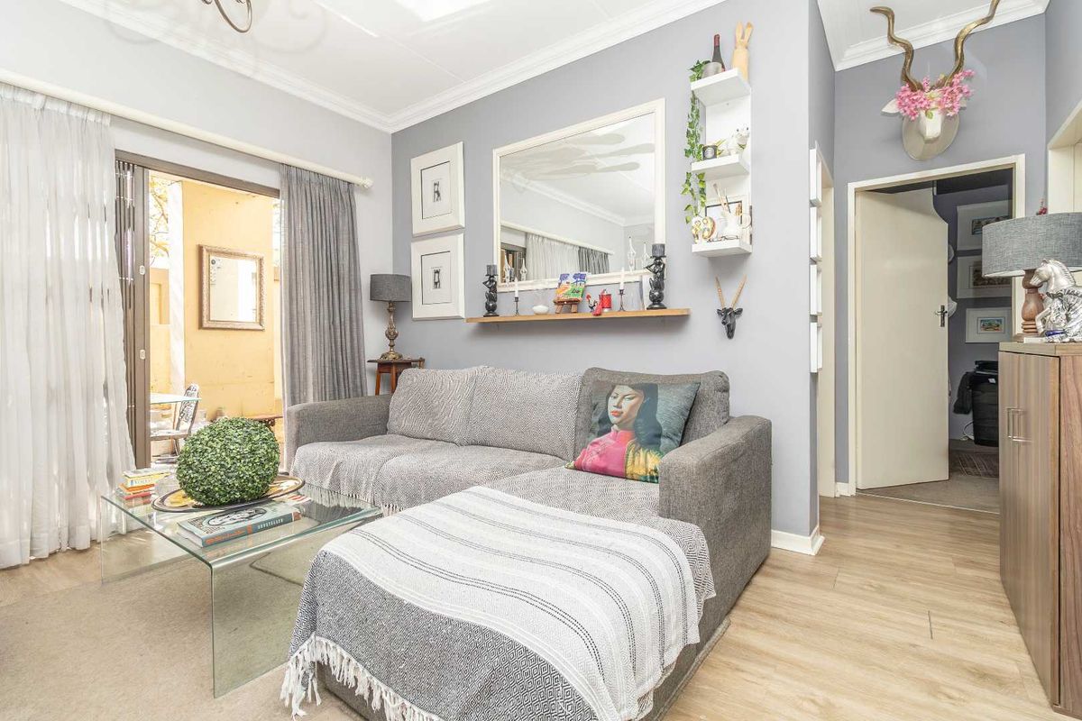 A well-maintained living room featuring light wood-look flooring, neutral grey walls, and sliding glass doors that provide access to an outdoor patio area.