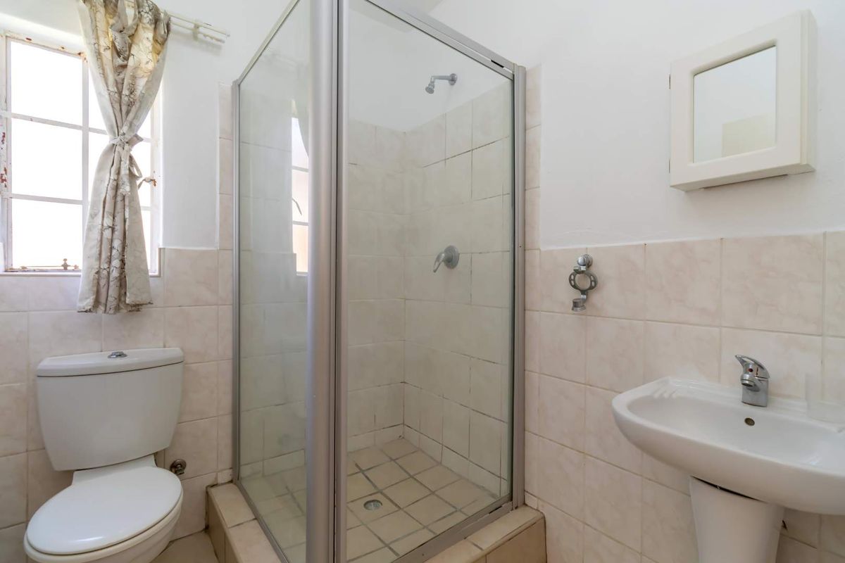A functional bathroom featuring a glass-enclosed shower, pedestal basin, and toilet with neutral wall and floor tiling.