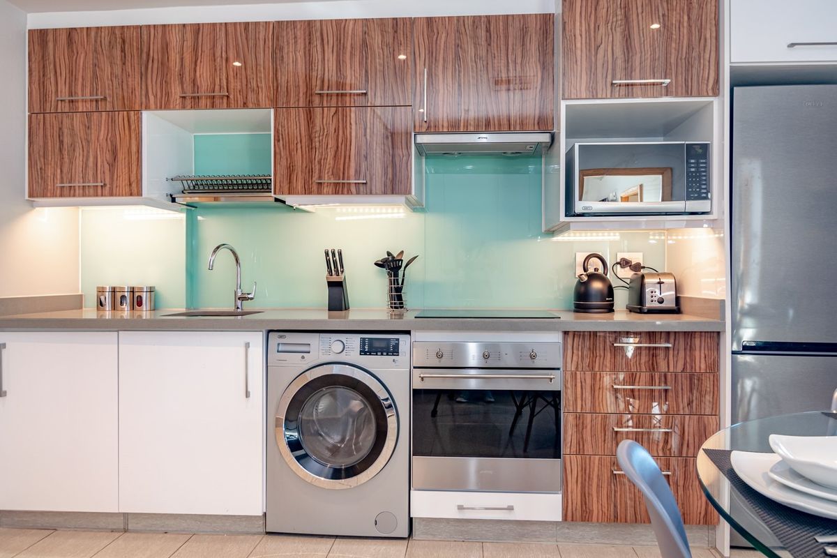 Modern kitchen featuring wood-grain cabinetry, stone countertops, a glass splashback, and integrated appliances including an oven, hob, and washing machine.