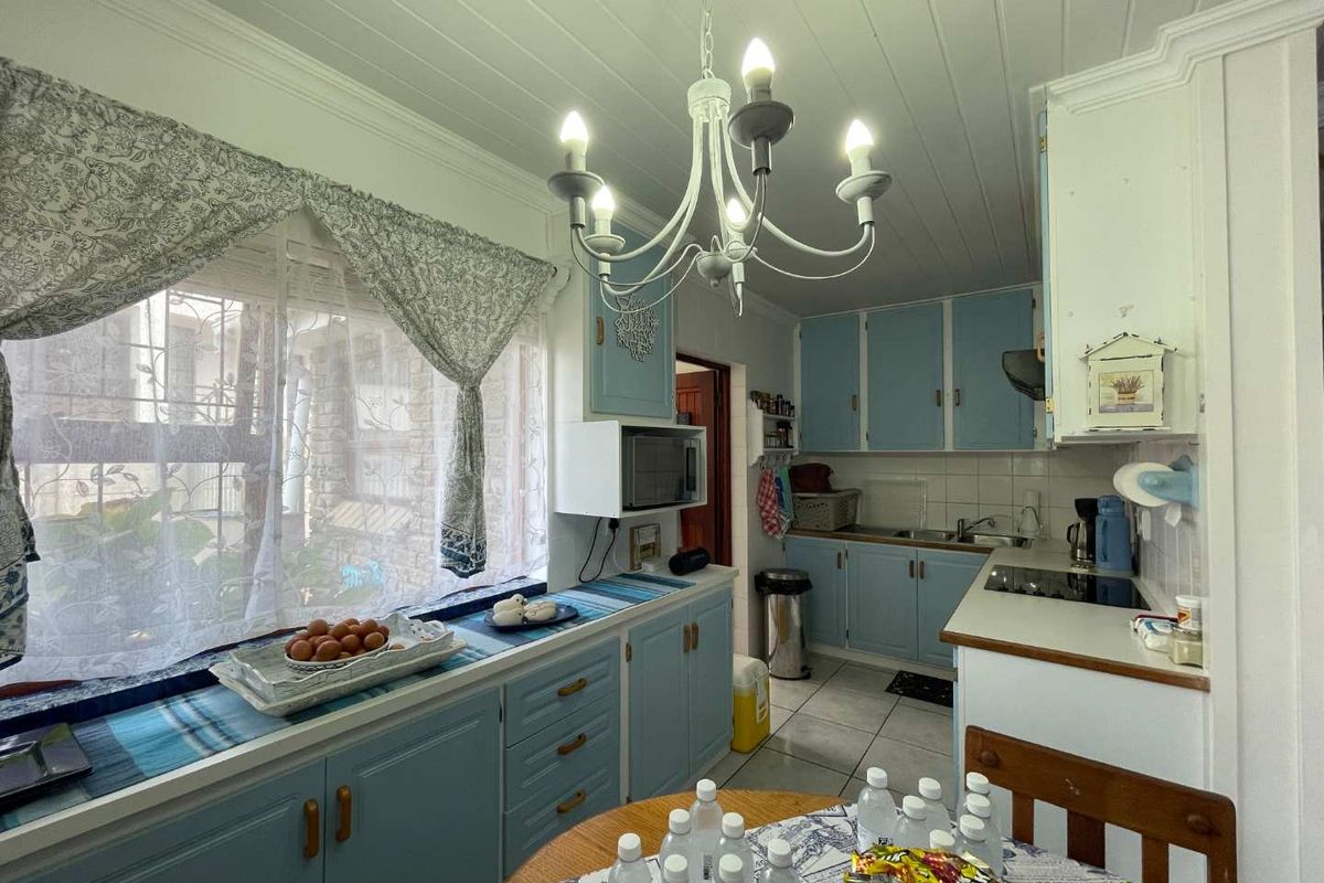A functional kitchen featuring light blue cabinetry, tiled flooring, a tiled backsplash, and a classic chandelier, offering a traditional aesthetic with potential for modernization.