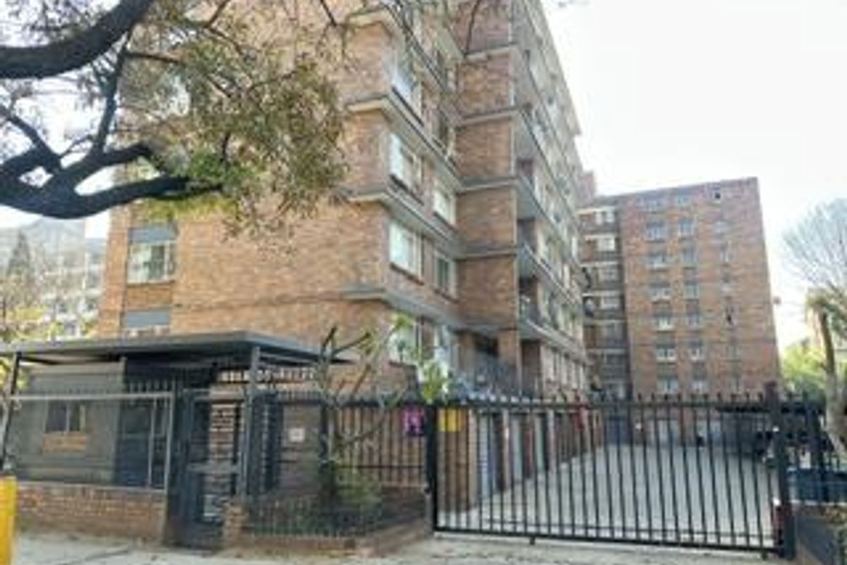 Exterior view of a multi-story brick apartment building featuring a secure gated entrance and perimeter fencing.