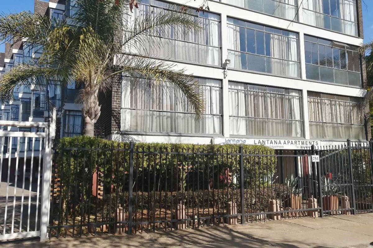 Front elevation of Lantana Apartments featuring a multi-story brick facade with large sliding glass windows and secure perimeter fencing.