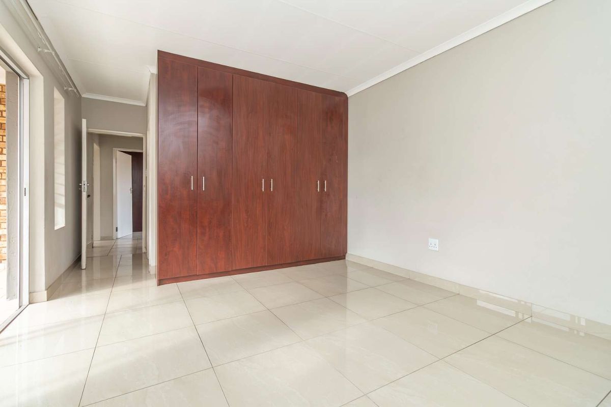 A bright bedroom featuring large format floor tiles and a substantial built-in wooden wardrobe with ample storage space.