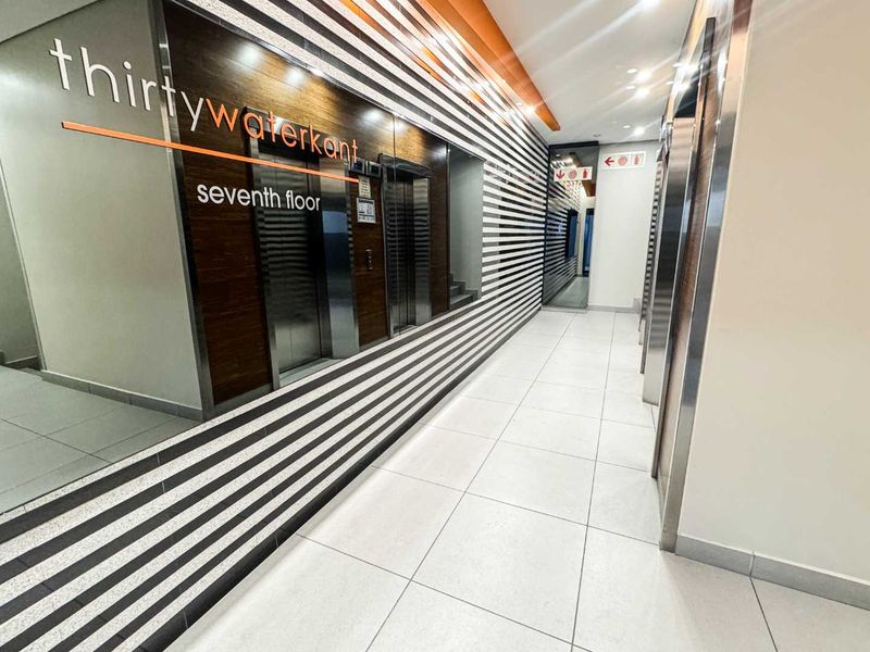 Modern office building elevator lobby featuring sleek tiled flooring, contemporary striped wall paneling, and stainless steel elevator doors on the seventh floor.