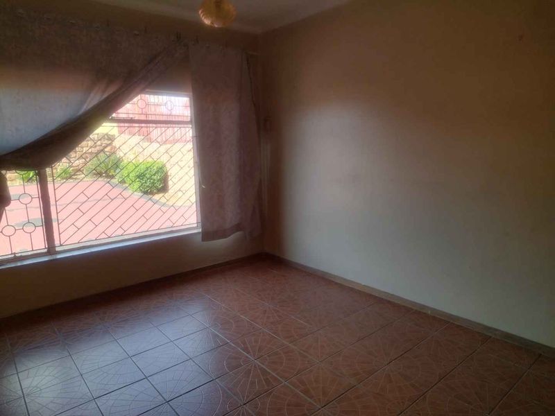 An empty living room featuring tiled flooring, a large window with security bars, and neutral wall finishes, offering a blank canvas for interior design.