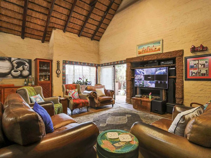 Spacious living room featuring a high vaulted thatched ceiling with exposed timber rafters, a rustic stone fireplace, and sliding glass doors leading outdoors.