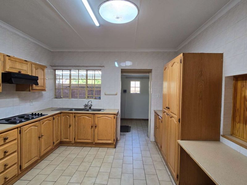 A functional kitchen featuring traditional wooden cabinetry, tiled splashbacks, and a built-in hob, offering a clean and practical layout for renovation.