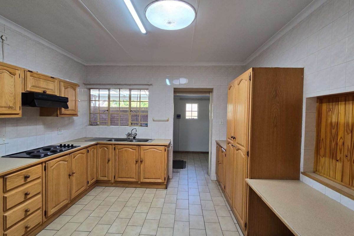 A functional kitchen featuring traditional wooden cabinetry, tiled splashbacks, and a built-in hob, offering a clean and practical layout for renovation.