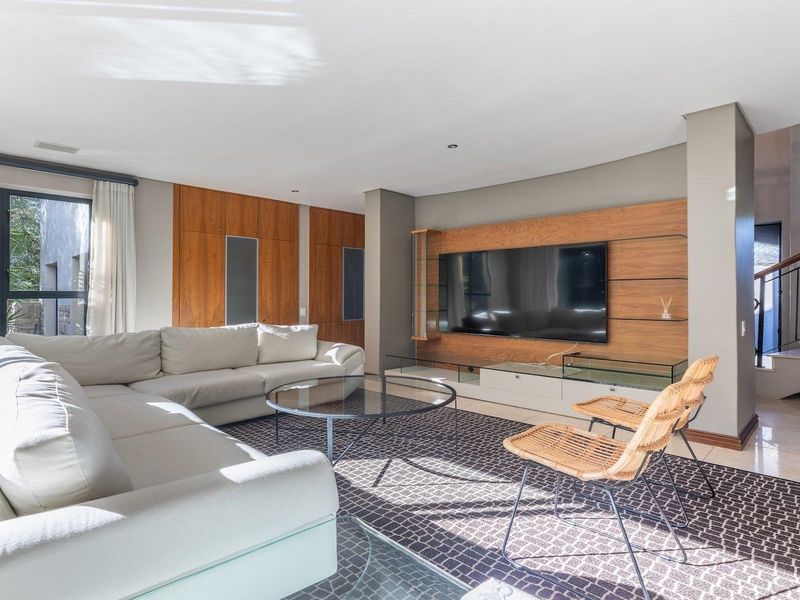 Spacious living room featuring a custom built-in wooden media wall, tiled flooring, and an elegant staircase with wrought iron detailing.