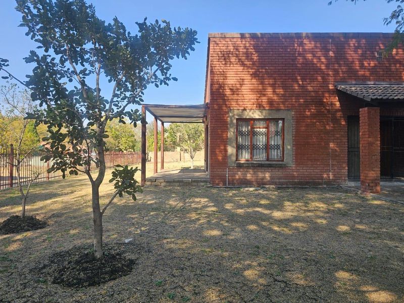 Rear view of a face brick house featuring a covered patio area, security window bars, and a spacious garden with perimeter fencing.