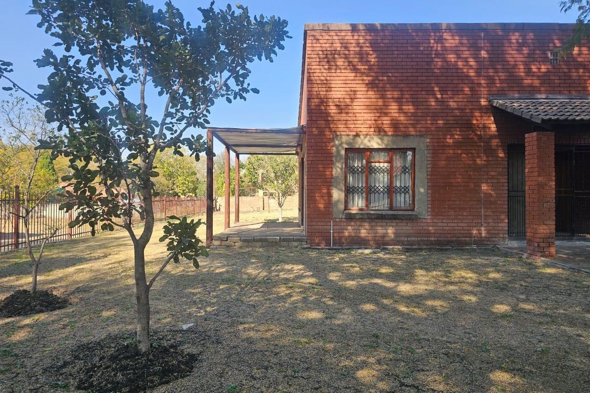 Rear view of a face brick house featuring a covered patio area, security window bars, and a spacious garden with perimeter fencing.
