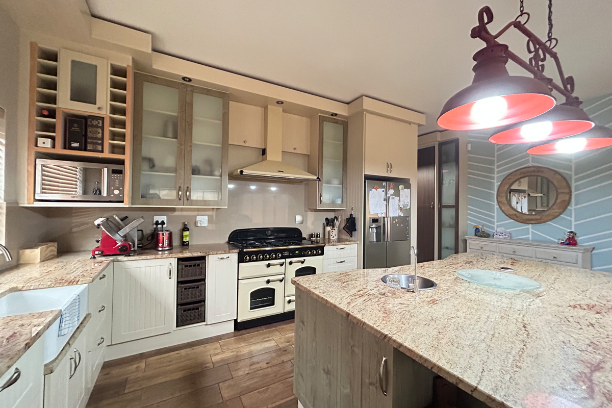 Spacious kitchen featuring a large central island with granite countertops, built-in oven, extractor fan, and ample cabinetry for storage.