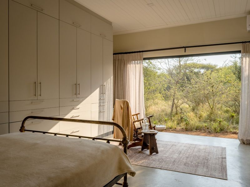 Spacious bedroom featuring extensive built-in cabinetry, polished concrete floors, and large sliding doors opening to a natural bushveld view.