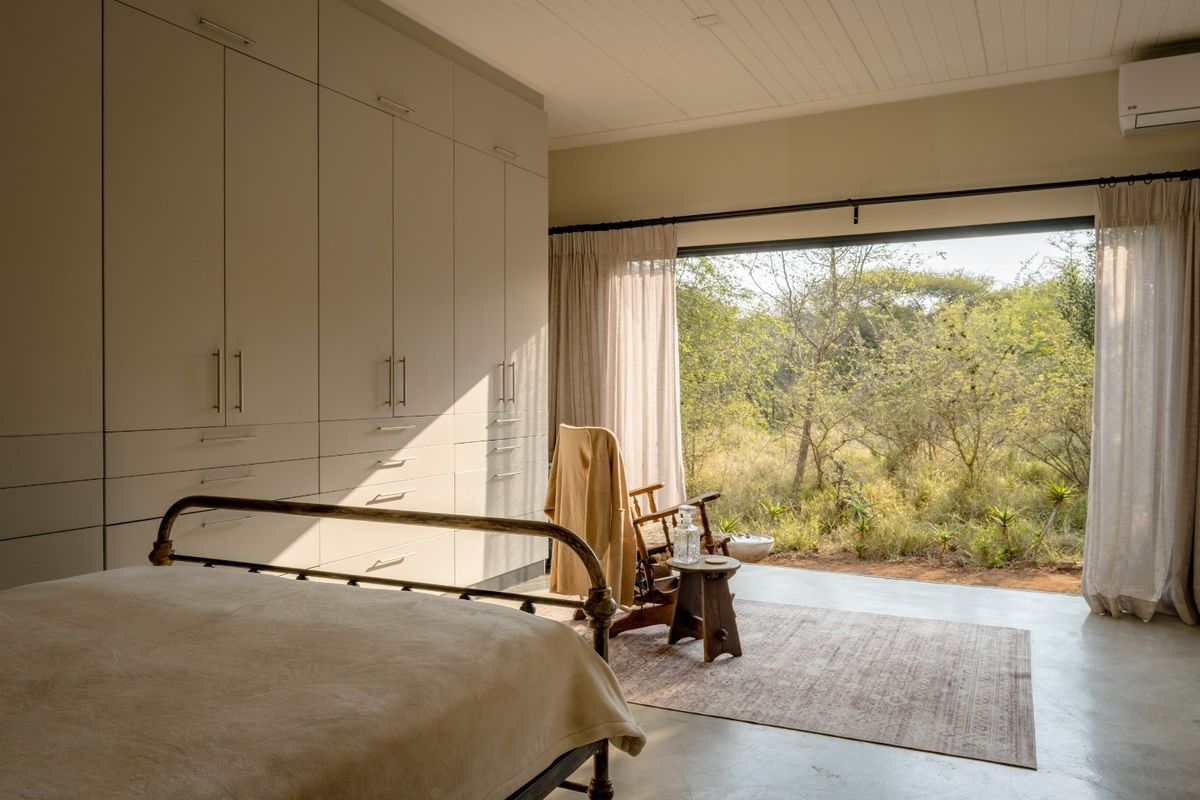 Spacious bedroom featuring extensive built-in cabinetry, polished concrete floors, and large sliding doors opening to a natural bushveld view.