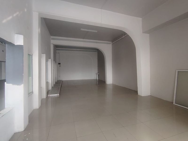 A spacious, empty open-plan commercial area featuring tiled flooring and distinctive arched structural columns, suitable for various business or retail configurations.