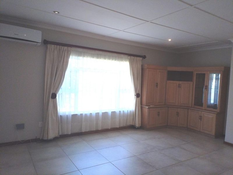 Spacious living area featuring neutral tiled flooring, built-in wooden cabinetry, and a wall-mounted air conditioning unit.