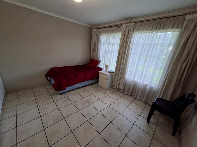 A simple bedroom featuring tiled flooring and large windows with curtain rails, offering a functional space ready for personalization.