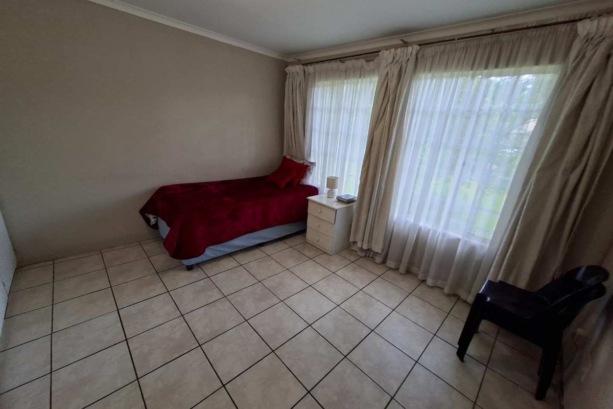 A simple bedroom featuring tiled flooring and large windows with curtain rails, offering a functional space ready for personalization.
