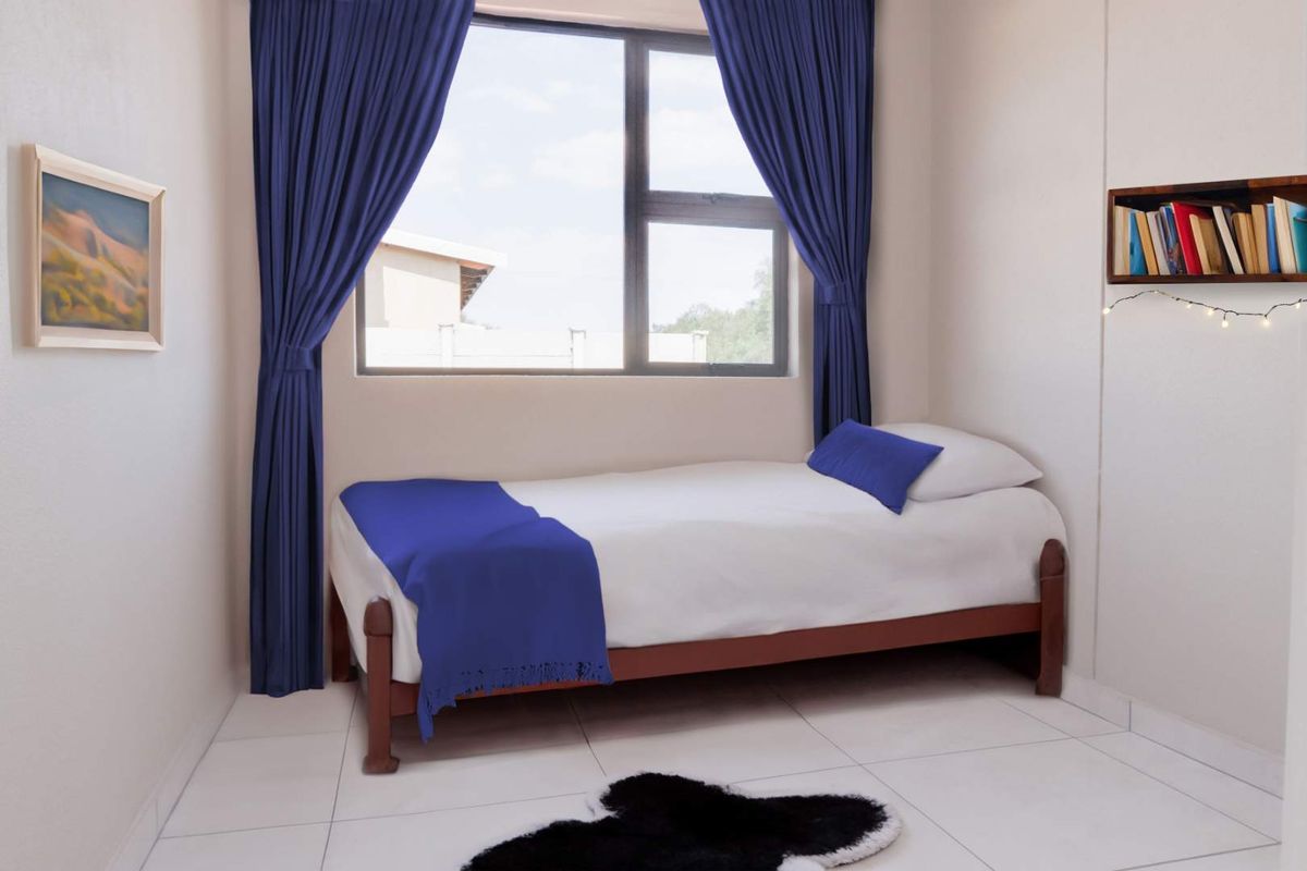 A compact bedroom featuring neutral tiled flooring and a large window with natural light, providing a clean and functional living space.