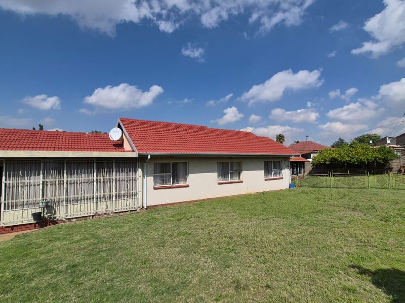 Rear view of the house featuring a tiled roof, security bars on windows, and a spacious backyard with perimeter fencing.