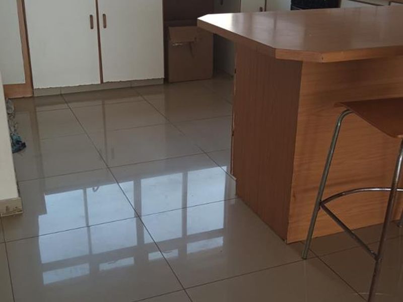 A dated kitchen featuring tiled flooring, laminate countertops, a breakfast bar, and built-in cabinetry with some visible wear and missing components.